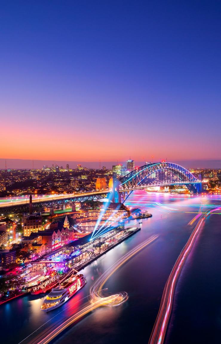 Luftaufnahme einer Hafenstadt geschmückt mit Regenbogenlichtern während Vivid Sydney, Sydney, New South Wales © Destination NSW Luftaufnahme einer Hafenstadt geschmückt mit Regenbogenlichtern während Vivid Sydney, Sydney, New South Wales © Destination NSW