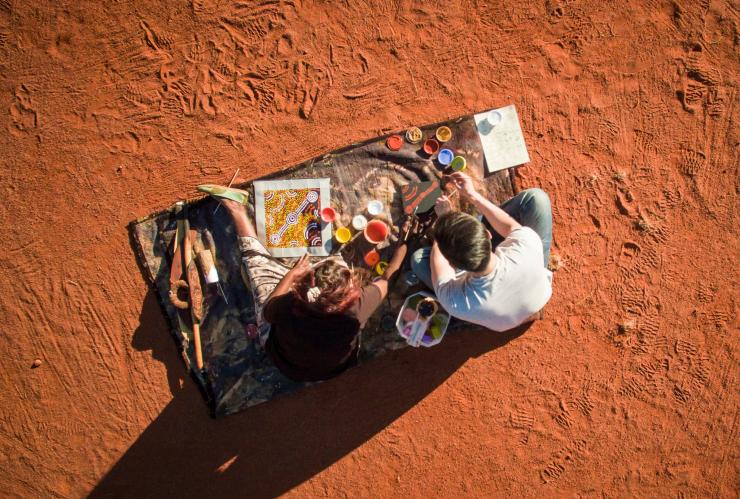 Ein Reisender, der bei einem einheimischen Aborigine-Künstler von Maruku Arts in der Nähe des Uluru Dotpainting lernt © Tourism NT/Archie Sartracom Ein Reisender, der bei einem einheimischen Aborigine-Künstler von Maruku Arts in der Nähe des Uluru Dotpainting lernt © Tourism NT/Archie Sartracom