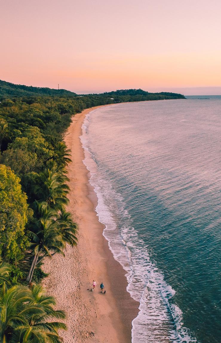 Luftaufnahme von zwei Personen, die bei Sonnenuntergang in Cairns am Sandstrand von Clifton Beach zwischen dem Regenwald und dem Ozean spazieren gehen, Queensland © Tourism and Events Queensland Luftaufnahme von zwei Personen, die bei Sonnenuntergang in Cairns am Sandstrand von Clifton Beach zwischen dem Regenwald und dem Ozean spazieren gehen, Queensland © Tourism and Events Queensland