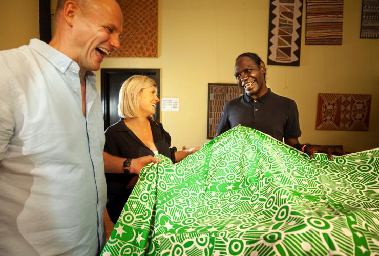 Buffy Warlapinni, an Aboriginal artist showing printed green fabric to two guests at Tiwi by Design, Tiwi Islands, Northern Territory © Tourism Australia