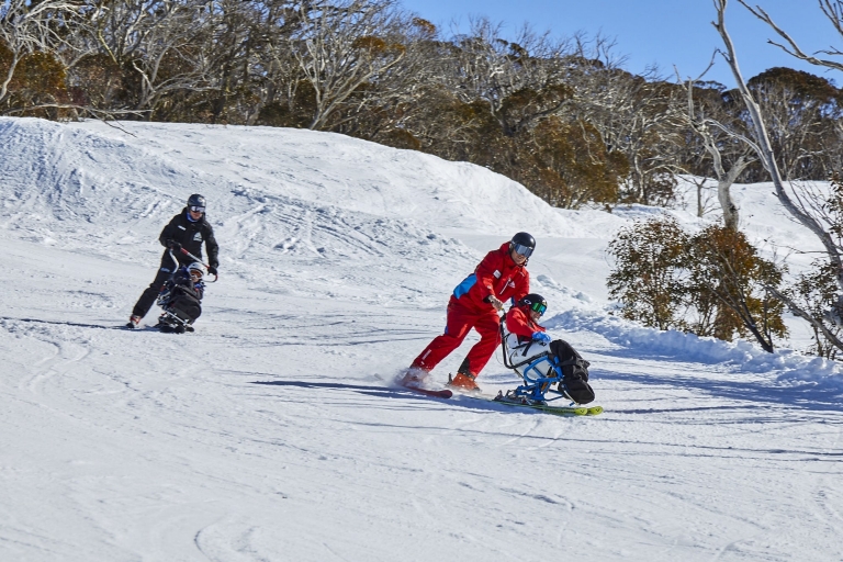 Two people with limited mobility adaptive skiing with instructors down a snow-covered mountain in Thredbo, Snowy Mountains, New South Wales © Tourism Australia Two people with limited mobility adaptive skiing with instructors down a snow-covered mountain in Thredbo, Snowy Mountains, New South Wales © Tourism Australia