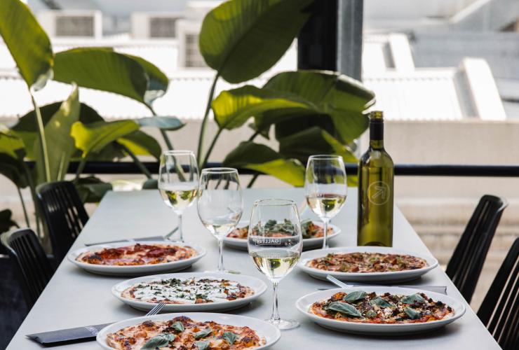 A table beside a window and green, leafy plant set with an assortment of pizzas and glasses of white wine at Gallery Bar, Adelaide, South Australia © Lewis Potter/Gallery Bar A table beside a window and green, leafy plant set with an assortment of pizzas and glasses of white wine at Gallery Bar, Adelaide, South Australia © Lewis Potter/Gallery Bar
