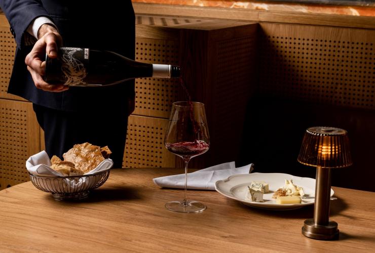 A waiter pouring a glass of red wine at a table set with a cheese plate and bread at Reine & La Rue, Melbourne, Victoria © Reine & La Rue A waiter pouring a glass of red wine at a table set with a cheese plate and bread at Reine & La Rue, Melbourne, Victoria © Reine & La Rue