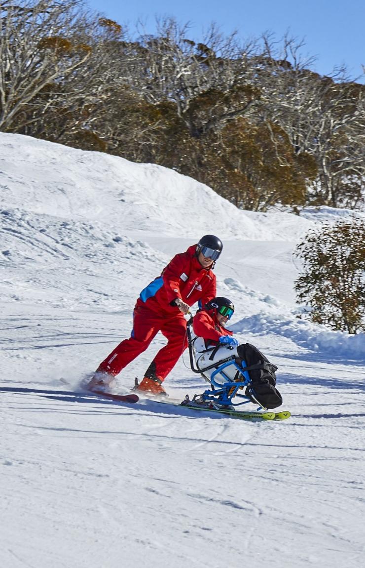 Two people with limited mobility adaptive skiing with instructors down a snow-covered mountain in Thredbo, Snowy Mountains, New South Wales © Tourism Australia Two people with limited mobility adaptive skiing with instructors down a snow-covered mountain in Thredbo, Snowy Mountains, New South Wales © Tourism Australia