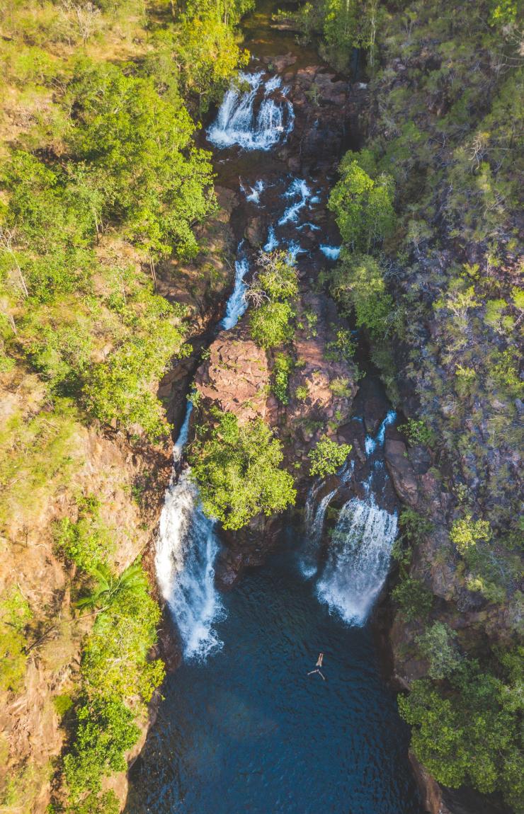 Aerial view over a person floating in a natural blue pool surrounded by trees with two large waterfalls cascading down at Florence Falls, Litchfield National Park, Northern Territory © Tourism NT/Dan Moore Aerial view over a person floating in a natural blue pool surrounded by trees with two large waterfalls cascading down at Florence Falls, Litchfield National Park, Northern Territory © Tourism NT/Dan Moore