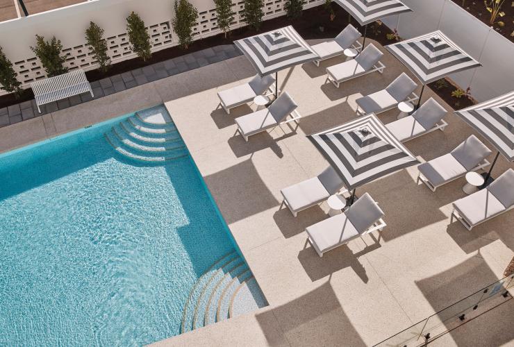 Aerial view over a blue pool surrounded by white tiles with white lounge chairs shaded by striped umbrellas at Hotel Alba, Adelaide, South Australia © South Australian Tourism Commission Aerial view over a blue pool surrounded by white tiles with white lounge chairs shaded by striped umbrellas at Hotel Alba, Adelaide, South Australia © South Australian Tourism Commission