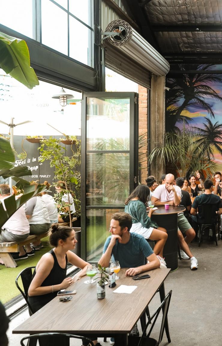 A crowd of people sitting around long tables in a brewery with a colourful mural. at One Drop Brewing, Botany, Sydney, New South Wales © One Drop Brewing Co.  A crowd of people sitting around long tables in a brewery with a colourful mural. at One Drop Brewing, Botany, Sydney, New South Wales © One Drop Brewing Co.