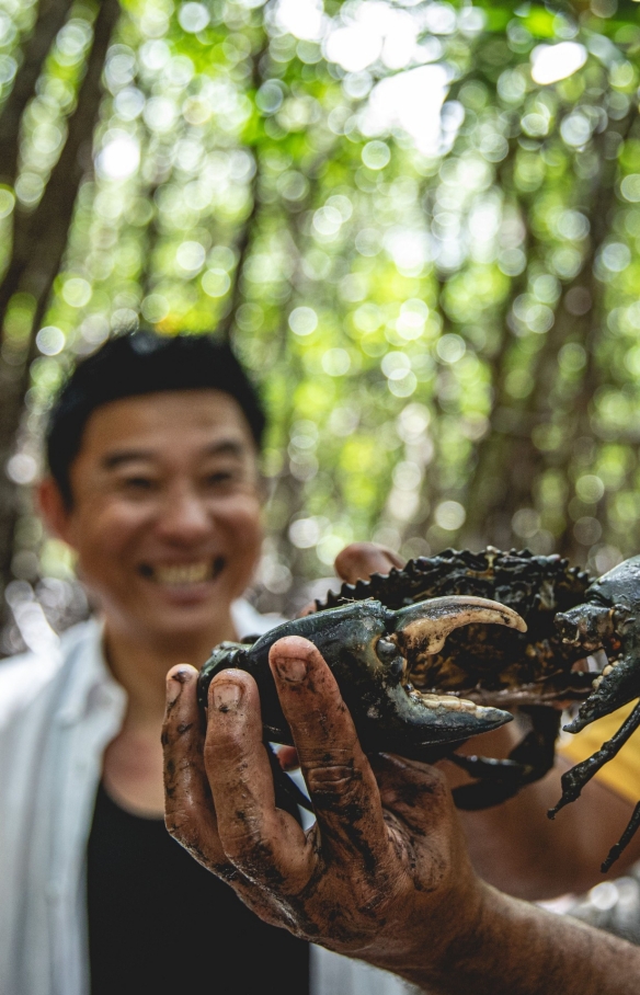 An Indigenous guide holding up a mud crab as a tour participant smiles widely behind him, Walkabout Cultural Adventures, Daintree Rainforest, Queensland © Tourism and Events Queensland