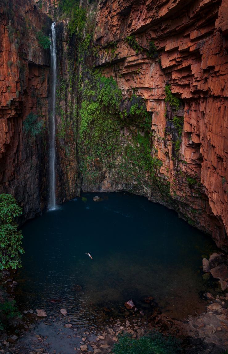 Vue aérienne d'une personne flottant sur le dos dans un point d'eau bleue entouré d'immenses parois rocheuses rouges ornées de mousse et d'une petite cascade à Emma Gorge, El Questro Wilderness Park, Kimberley, Australie Occidentale © Tourism Australia Vue aérienne d'une personne flottant sur le dos dans un point d'eau bleue entouré d'immenses parois rocheuses rouges ornées de mousse et d'une petite cascade à Emma Gorge, El Questro Wilderness Park, Kimberley, Australie Occidentale © Tourism Australia