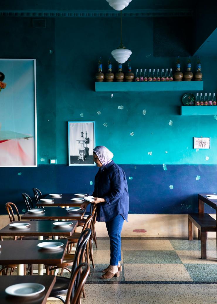 Seorang wanita menata meja di ruang berwarna biru di Parwana Afghan Kitchen, Adelaide, South Australia © Josie Withers