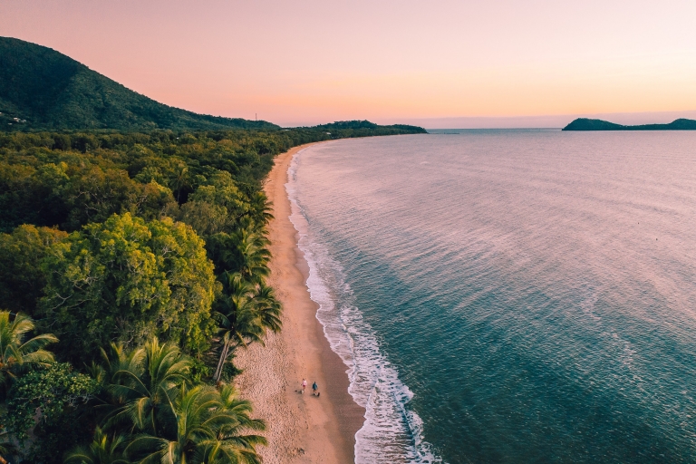 Pemandangan dari udara dua orang berjalan kaki di sepanjang hamparan pasir Clifton Beach di antara hutan hujan dan samudra saat matahari terbenam di Cairns, Queensland © Tourism and Events Queensland Pemandangan dari udara dua orang berjalan kaki di sepanjang hamparan pasir Clifton Beach di antara hutan hujan dan samudra saat matahari terbenam di Cairns, Queensland © Tourism and Events Queensland