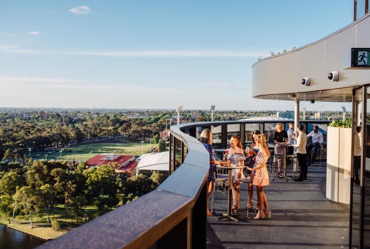 Gruppo di amici che sorseggiano un drink intorno a un tavolo su una terrazza affacciata sui sobborghi e sul bushland al SOL Rooftop, Adelaide, South Australia © Meaghan Coles Gruppo di amici che sorseggiano un drink intorno a un tavolo su una terrazza affacciata sui sobborghi e sul bushland al SOL Rooftop, Adelaide, South Australia © Meaghan Coles