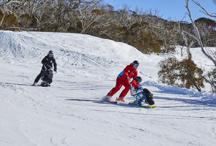 Istruttore di sci che assiste uno sciatore adattivo lungo la montagna, Thredbo Alpine Village, Snowy Mountains, New South Wales © Tourism Australia