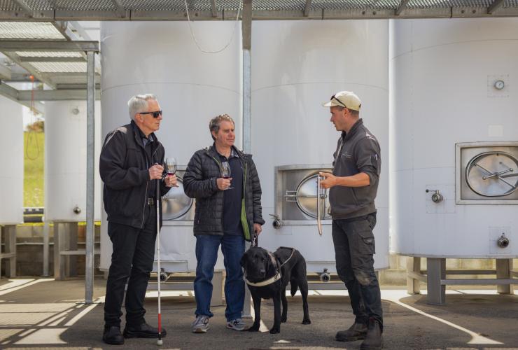 Uomo con un cane guida che degusta vino con un amico e una guida al Puddleduck Vineyard, Richmond, Tasmania © Dearna Bond