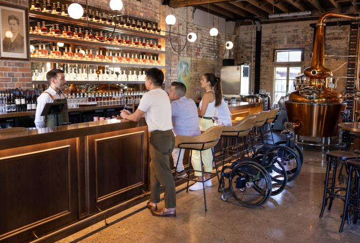 Amici seduti a degustare distillati al distretto Rivermakers con una sedia a rotelle accanto, Brisbane, Queensland © Tourism and Events Queensland