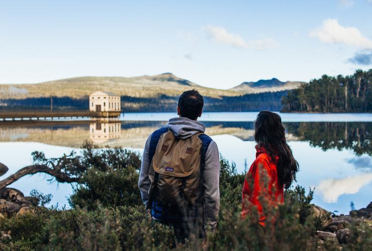 Ein Paar an einem Aussichtspunkt am Lake St Clair mit Pumphouse Point in der Ferne, Lake St Clair, Tasmanien © Adam Gibson