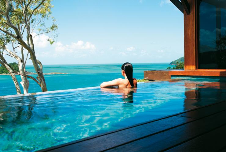 Eine Frau lehnt am Rand eines Infinity-Pools mit Blick auf den Ozean am qualia, Hamilton Island, Queensland © Jason Loucas Photography