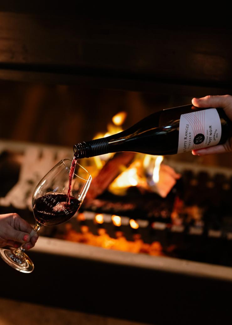 Vor einem Feuer im Mt Lofty Ranges Vineyard wird Rotwein in ein Glas ausgeschenkt, Adelaide Hills, Südaustralien © South Australian Tourism Commission