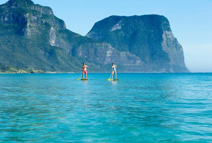 Ein Mann und eine Frau beim Stand-Up-Paddeln auf dem strahlend blauen Wasser vor Lord Howe Island, New South Wales © Destination NSW
