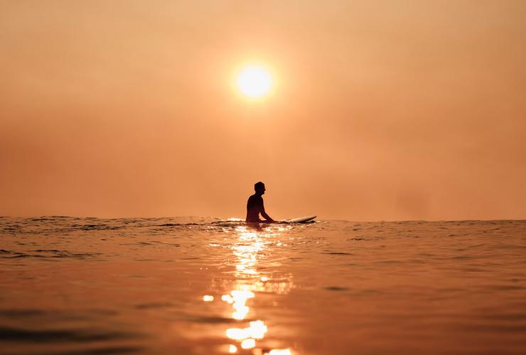 Silhouette d'un surfeur assis sur une planche de surf devant un coucher de soleil orange à Bondi Beach, Sydney, Nouvelle-Galles du Sud © Tourism Australia
