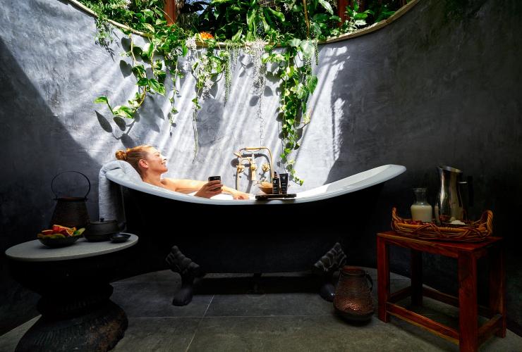Une femme se relaxant dans une baignoire de plein-air, sous des feuilles de vignes vertes tombant le long du mur, éclairée par un rayon de soleil, à Gaia Retreat & Spa, Byron Bay, Nouvelle-Galles du Sud © Gaia Retreat & Spa