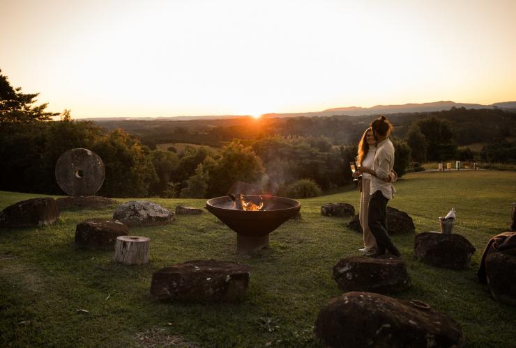 Un couple debout près d'un feu de camp sur une colline verdoyante lors du coucher de soleil à Gaia Retreat & Spa, Byron Bay, Nouvelle-Galles du Sud © Gaia Retreat & Spa