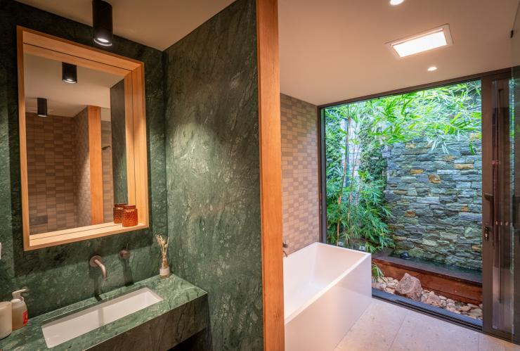 L'intérieur de la salle de bain d'un hébergement de Samadhi Retreat arborant du marbre vert, et dotée d'une baignoire et d'une fenêtre panoramique donnant sur le bush verdoyant, Daylesford, Victoria, © Samadhi Retreat