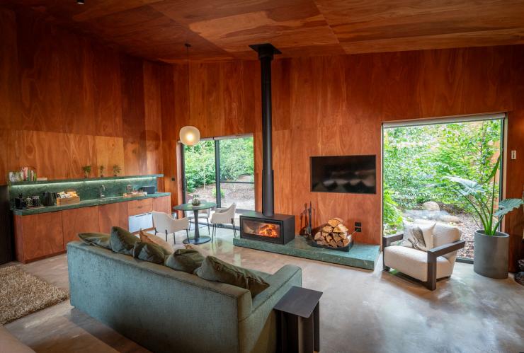 L'intérieur d'un hébergement de Samadhi Retreat doté d'un poêle à bois allumé placé entre des meubles verts et en bois à Daylesford, Victoria, © Samadhi Retreat