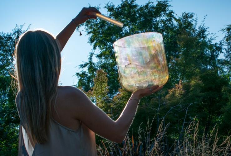 Une personne se trouvant à l'extérieur, dans le bush, un bol chantant et une baguette à la main, lors d'une journée ensoleillée à Samadhi Retreat, Daylesford, Victoria © Samadhi Retreat