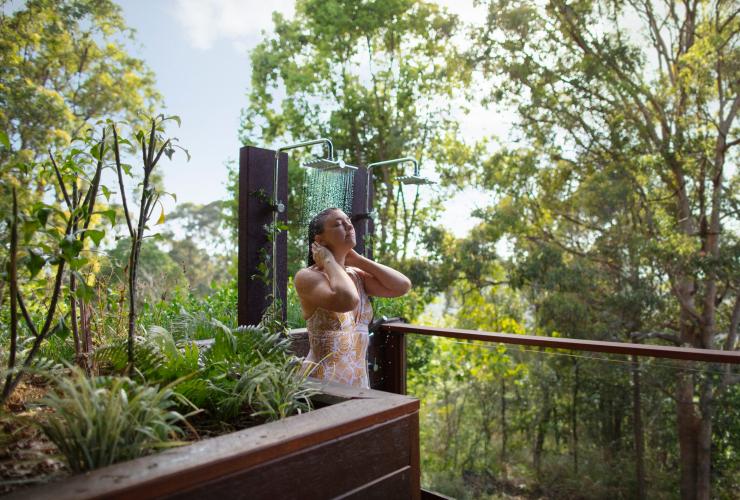Une femme prenant une douche de plein-air, entre les arbres et les plantes, lors d'une journée ensoleillée au Gwinganna Lifestyle Retreat, Gold Coast, Queensland © Destination Gold Coast