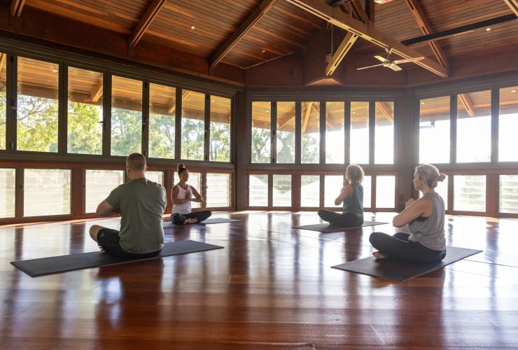 Trois touristes et une professeure pratiquant le yoga dans un studio dédié au Gwinganna Lifestyle Retreat, Gold Coast, Queensland © Tourism Australia