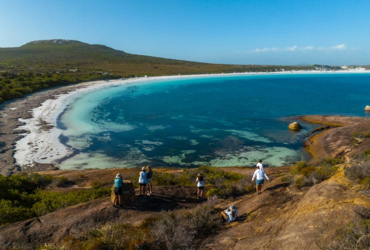 Un groupe de personnes sur un promontoire surplombant une plage de sable blanc bordée par un bush dense et une eau limpide lors d'une activité avec Untamed Escapes, Esperance, Australie Occidentale, © Tourism Australia