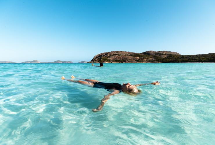 Une personne flottant sur l'eau claire et bleu vif de l'océan lors d'une journée ensoleillée avec Untamed Escapes, Esperance, Australie Occidentale, © Tourism Australia