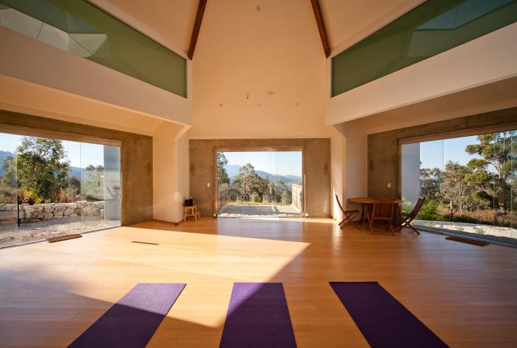 L'intérieur d'une salle baignée de lumière avec trois tapis de yoga violets posés sur le sol et des fenêtres offrant une vue imprenable sur le bush au Harmony Hill Health Retreat, Hobart, Tasmanie © Harmony Hill Health Retreat