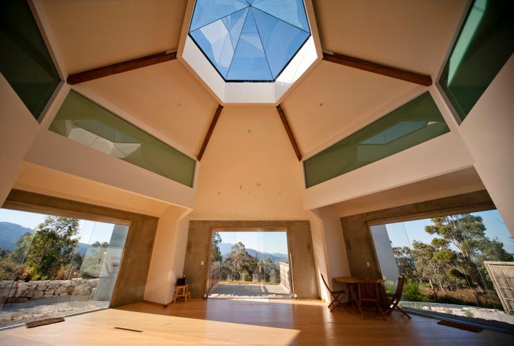 L'intérieur d'une salle de yoga baignée de lumière avec de grandes fenêtres et un toit hexagonal donnant sur les arbres situés à l'extérieur du Harmony Hill Health Retreat, Hobart, Tasmanie © Harmony Hill Health Retreat