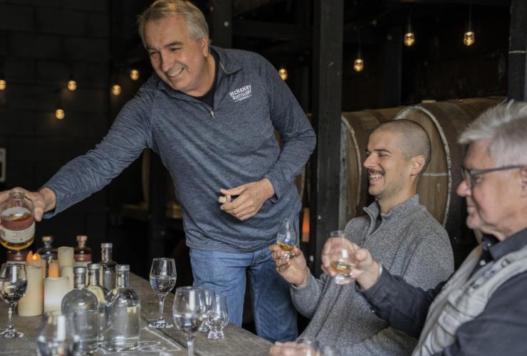 Seorang anggota staf menyajikan minuman beralkohol ke para tamu yang bersuka ria duduk mengelilingi meja di McHenry Distillery, Tasman Peninsula, Tasmania © Tourism Australia