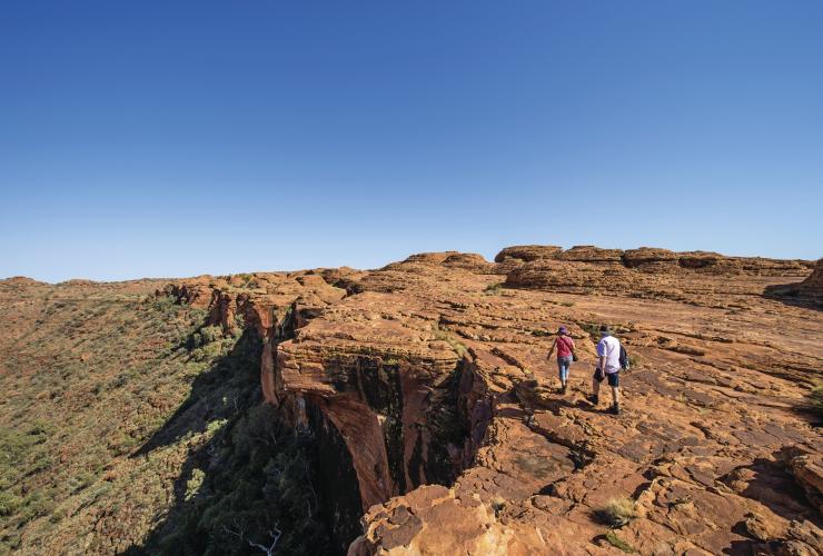 Dua orang berjalan di tepi tebing dengan padang semak di bawahnya di sepanjang Rim Walk, Kings Canyon, Northern Territory © Tourism Northern Territory/Shaana McNaught 