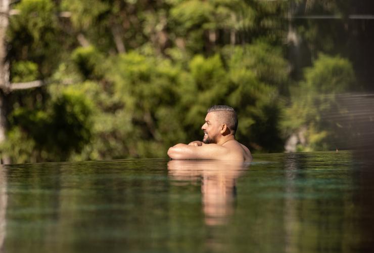 Un ospite appoggiato al bordo della piscina a sfioro tra gli alberi del Gwinganna Lifestyle Retreat, Gold Coast, Queensland © Tourism Australia