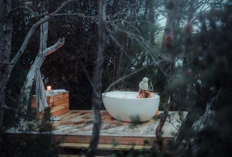 Donna che fa un bagno all'aperto tra gli alberi a The Retreat, Pumphouse Point, Lake St Clair, Tasmania © Emilie Ristevski