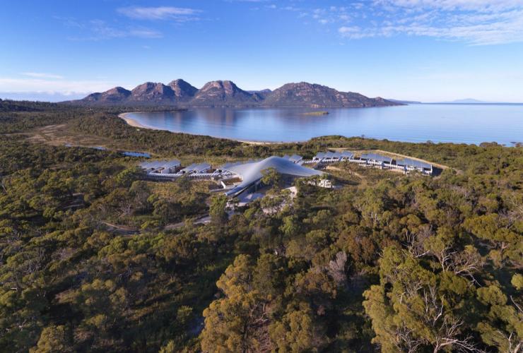 Vista aerea delle accomodation del Saffire Freycinet nascoste tra gli alberi, con Coles Bay e il Freycinet National Park sullo sfondo, Tasmania © Saffire Freycinet