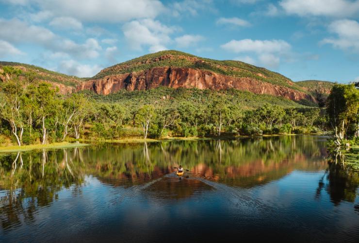 Persona che va in kayak su acque placide circondate da alberi e montagne rocciose in una giornata di sole al Mt. Mulligan Lodge, Mount Mulligan, Queensland © Mount Mulligan Lodge
